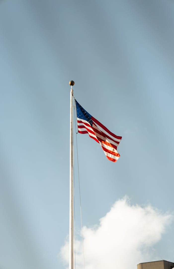 The American flag waving proudly on a tall flagpole, against a backdrop of a clear blue sky.